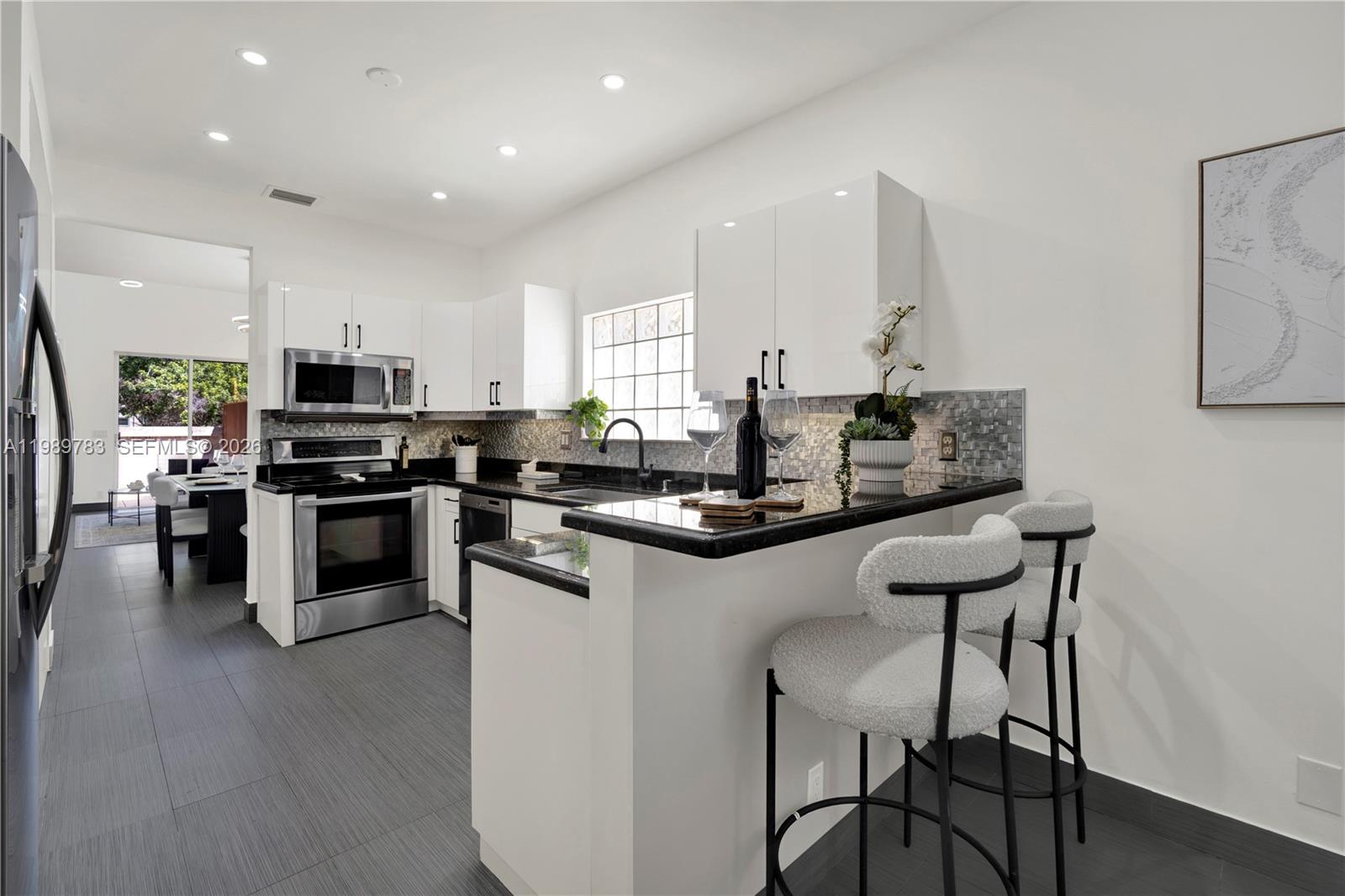 A modern kitchen features white cabinets, black countertops, stainless steel appliances, and two bar stools — 1251 Hayes St, Hollywood FL 33019, HOLLYWOOD, FL