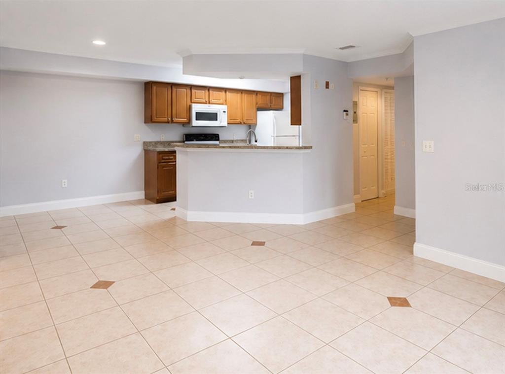 A kitchen with wood cabinets and a breakfast bar overlooks a tiled living area — 738 CREST PINES DRIVE UNIT 728, ORLANDO, FL