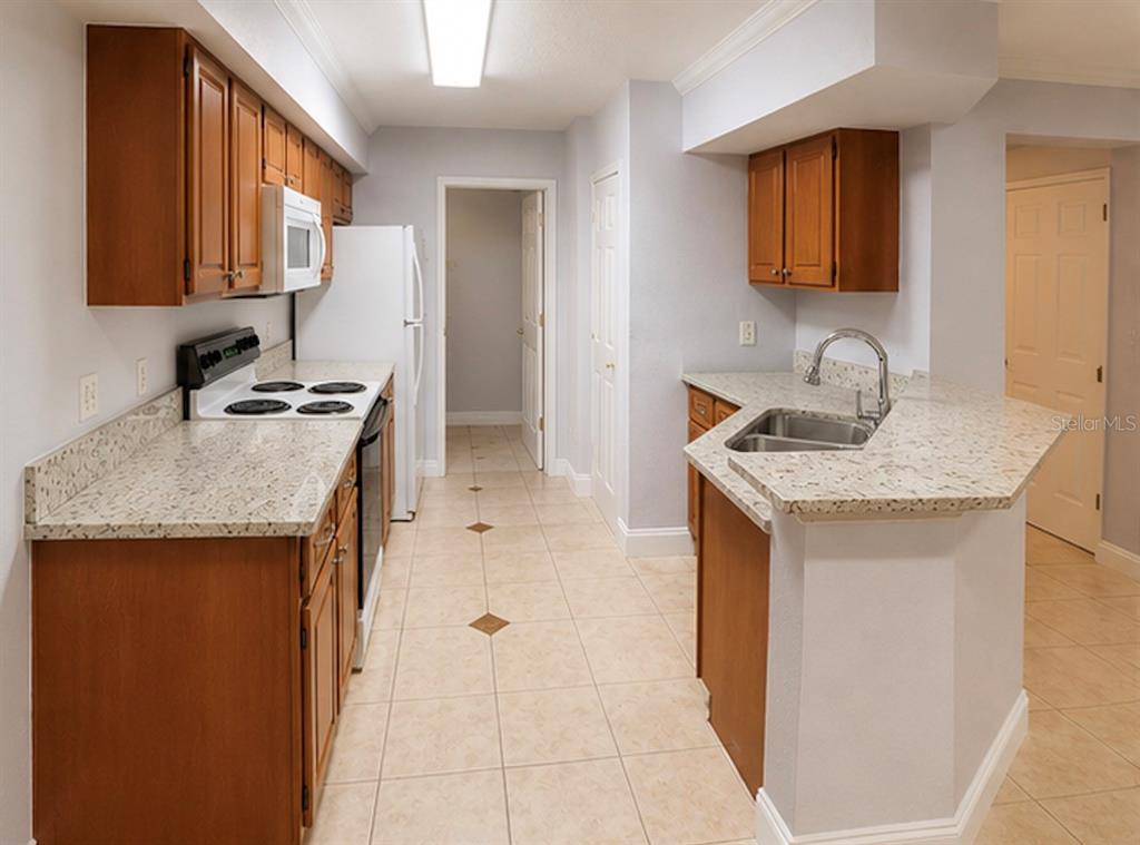 A kitchen features wood cabinets, light-colored granite countertops, white appliances, and beige tile flooring — 738 CREST PINES DRIVE UNIT 728, ORLANDO, FL