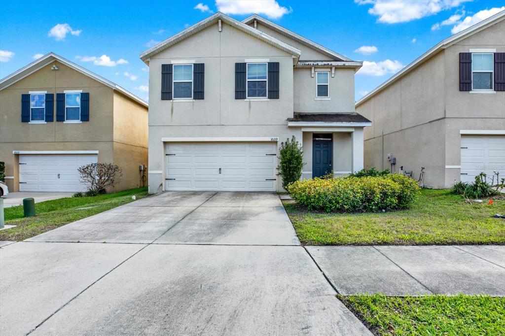 A two-story suburban house with a two-car garage, beige stucco siding, and a concrete driveway — 10219 HAWK STORM AVENUE, TAMPA, FL
