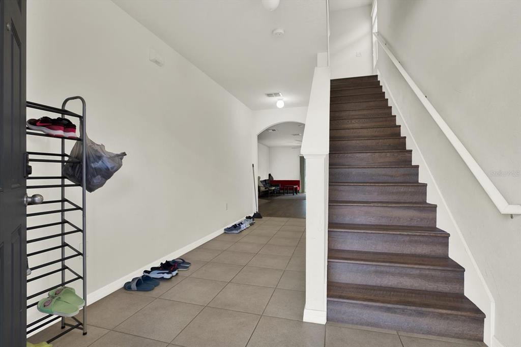 An entryway features tile flooring, a shoe rack, and a wooden staircase leading upstairs — 10219 HAWK STORM AVENUE, TAMPA, FL
