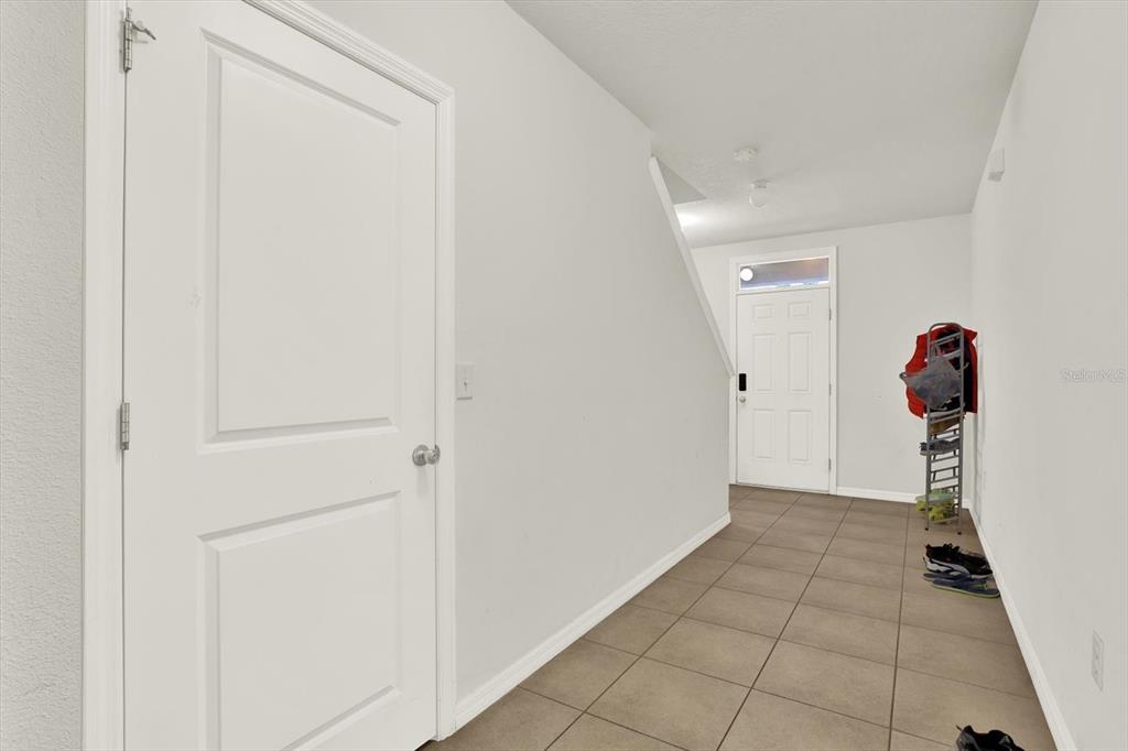 A tiled entryway features a white door, a staircase wall, and a metal shoe rack — 10219 HAWK STORM AVENUE, TAMPA, FL