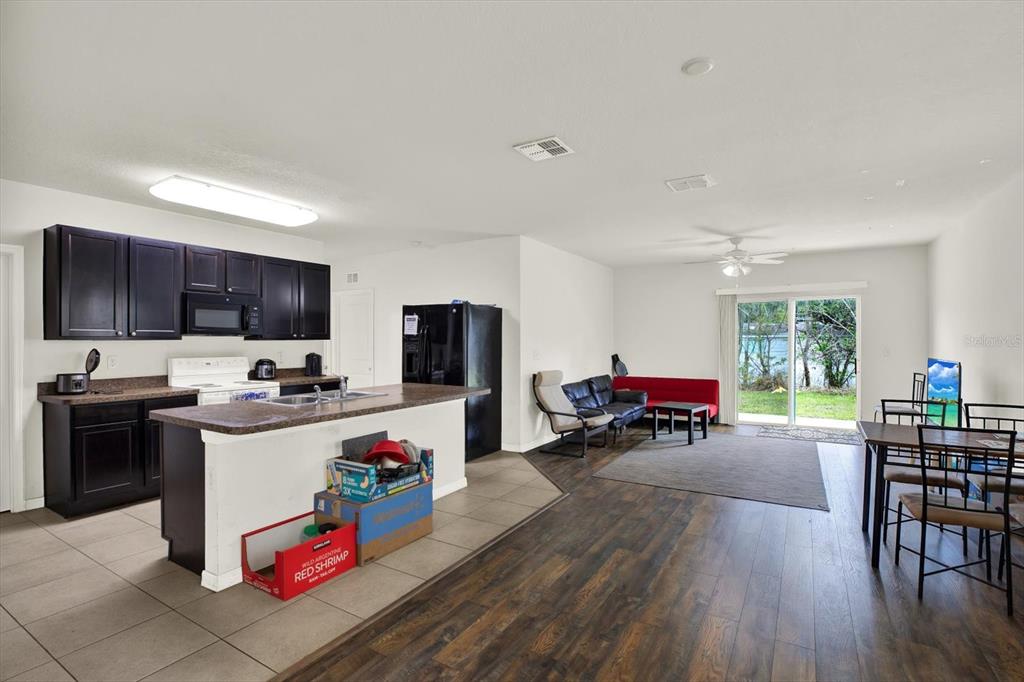 An open-concept kitchen and living area with dark cabinetry, a kitchen island, and sliding doors — 10219 HAWK STORM AVENUE, TAMPA, FL