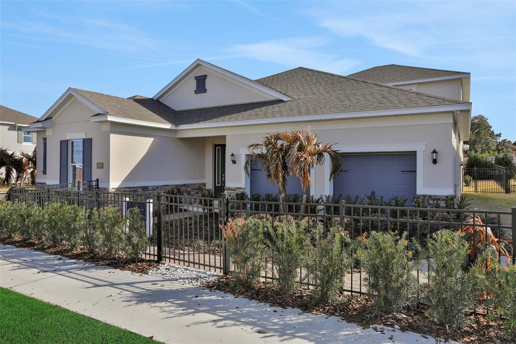 A single-story house with a beige exterior, stone accents, and a dark metal fence — 15136 TEA TREE DRIVE, WINTER GARDEN, FL
