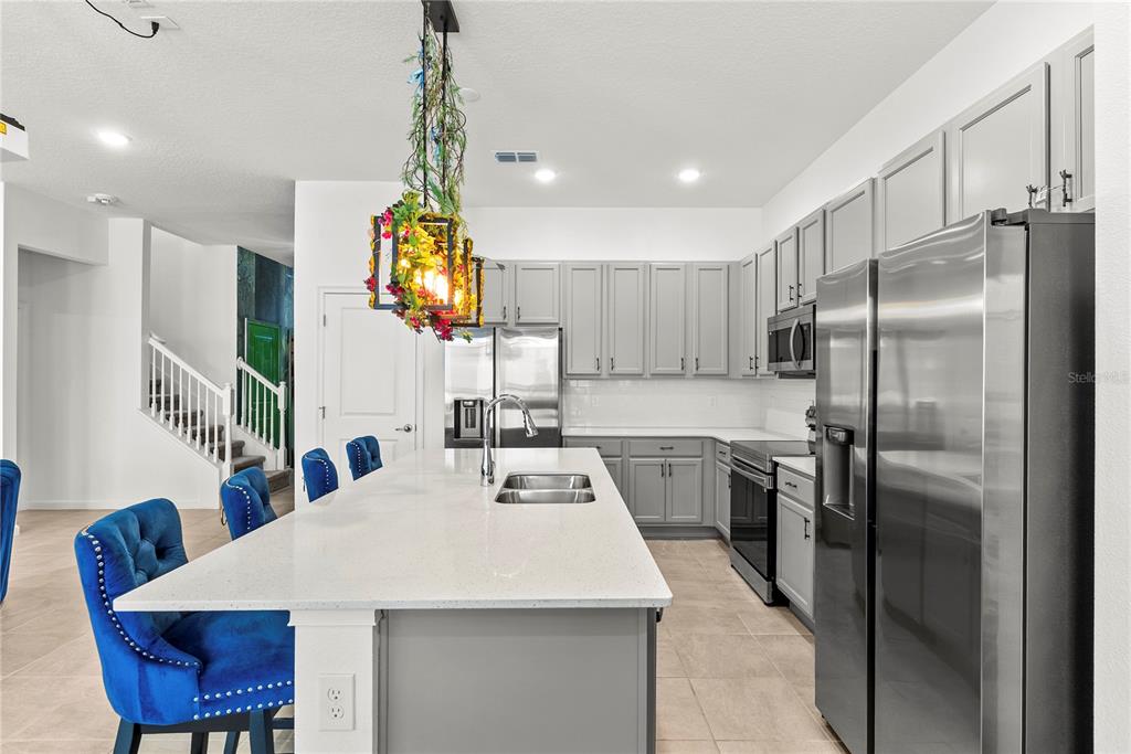 A kitchen features a large island with blue chairs, gray cabinetry, and stainless steel appliances — 5893 HIGH SEAS DRIVE, ORLANDO, FL
