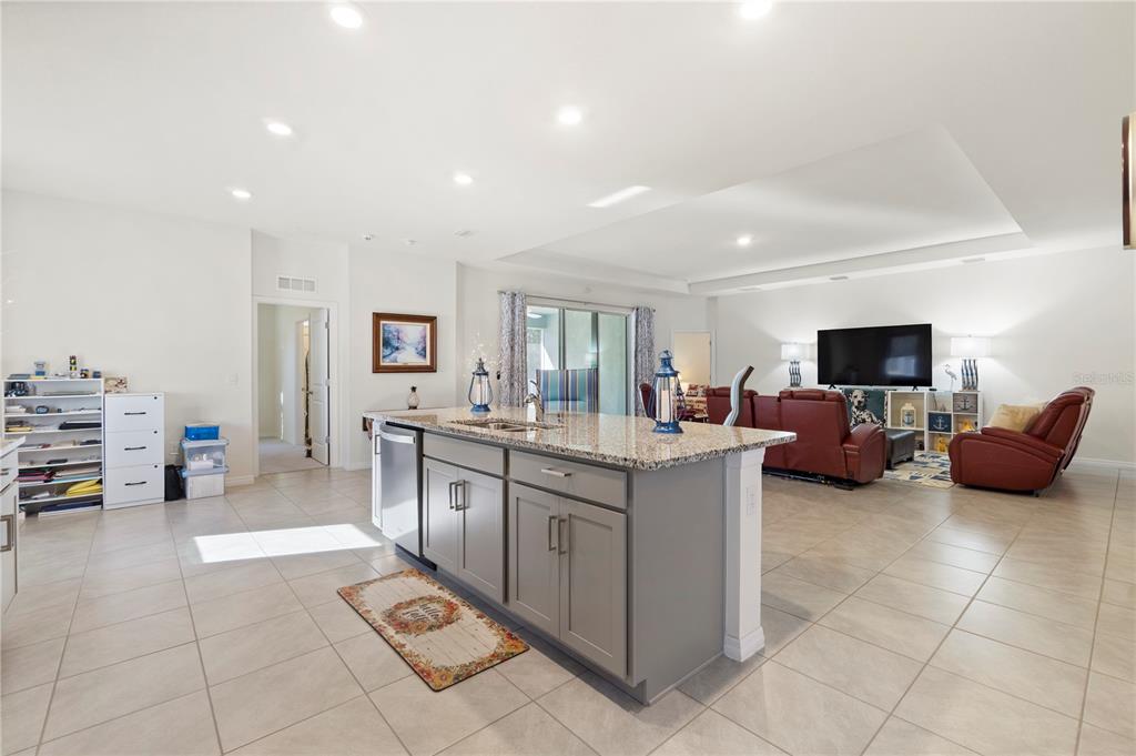 An open-concept kitchen with a gray island and granite countertops overlooks a living area — 1320 SE 63RD COURT ROAD, OCALA, FL