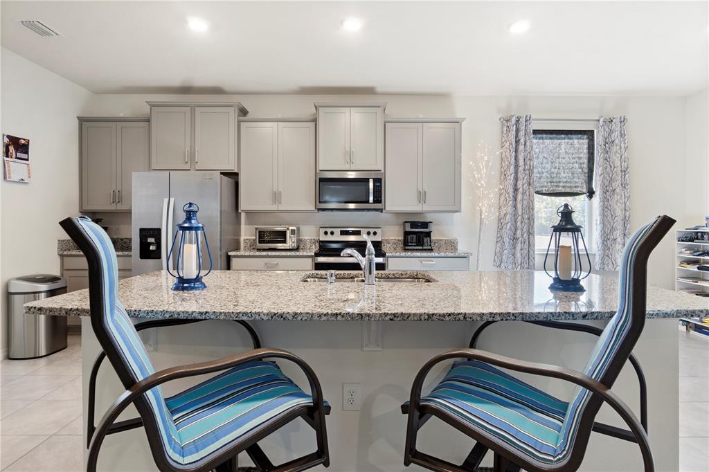 A kitchen features gray cabinets, stainless steel appliances, a granite island, and two striped chairs — 1320 SE 63RD COURT ROAD, OCALA, FL