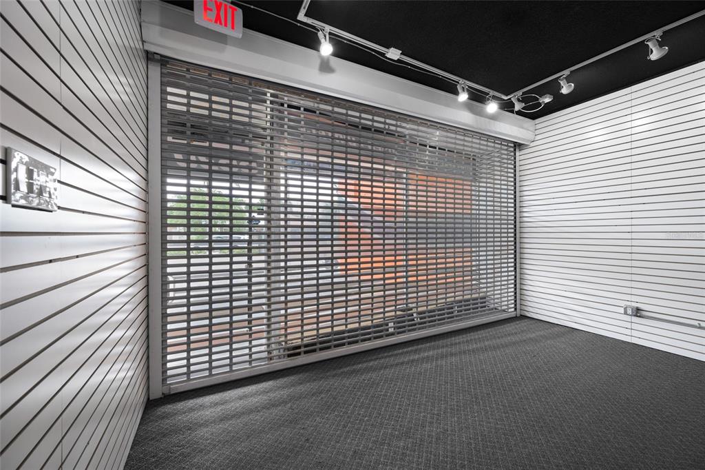 An empty retail space features white slat walls, gray carpet, and a metal security gate — 6630 GULF BOULEVARD, ST PETE BEACH, FL