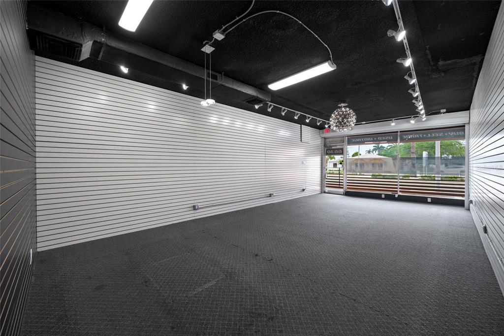 An empty commercial space features white slat walls, a dark carpeted floor, and exposed ceiling — 6630 GULF BOULEVARD, ST PETE BEACH, FL