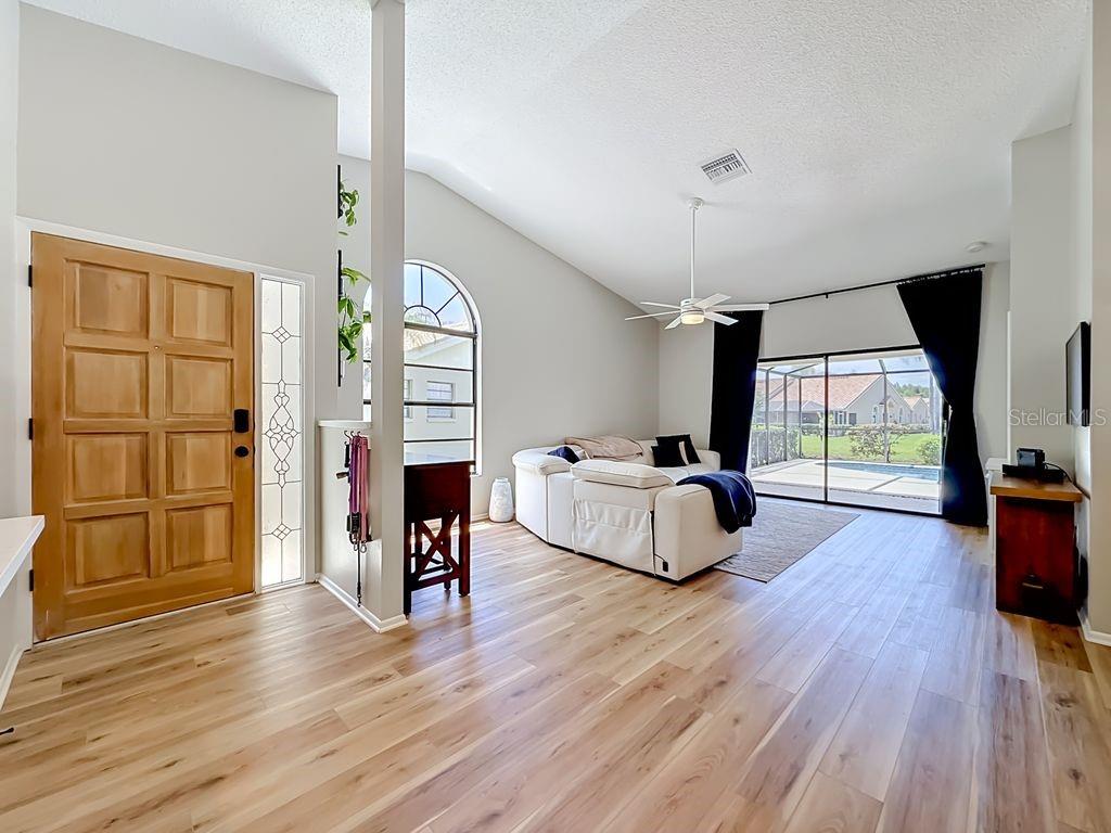 A living room features light wood flooring, a vaulted ceiling, and sliding doors to a pool — 5569 GREYSTON STREET, PALM HARBOR, FL