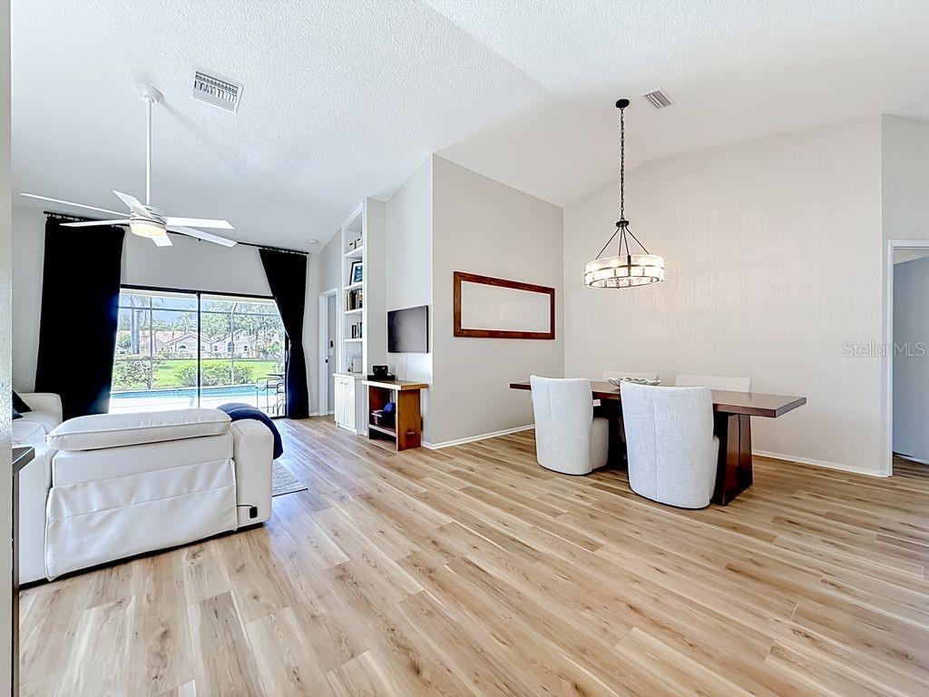 A dining area and living room with wood-look flooring, white furniture, and a sliding glass door — 5569 GREYSTON STREET, PALM HARBOR, FL