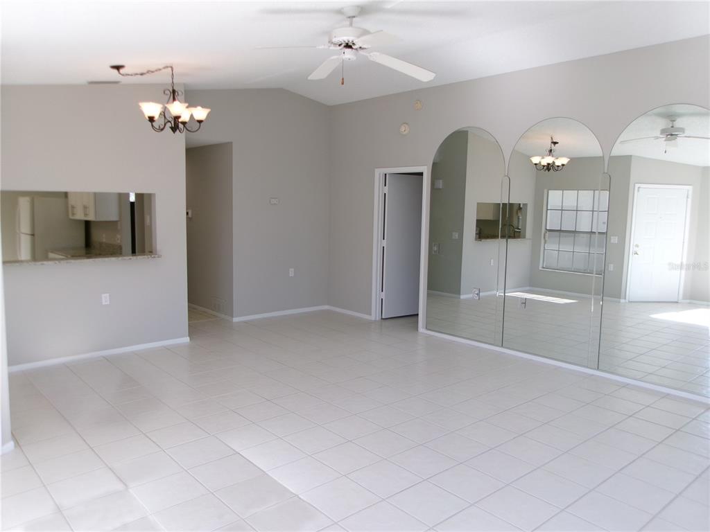 An open living area features white tile flooring, a ceiling fan, and large arched wall mirrors — 11604 VERSAILLES LANE, PORT RICHEY, FL