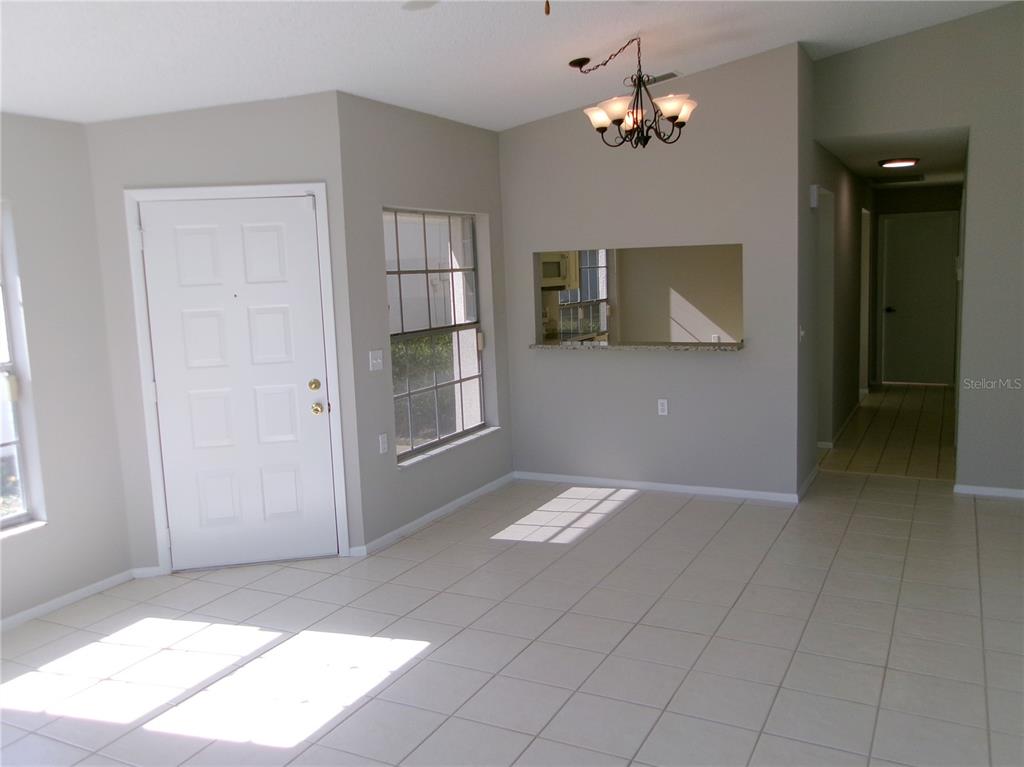 A dining area with tile flooring, a chandelier, a pass-through window, and an entry door — 11604 VERSAILLES LANE, PORT RICHEY, FL