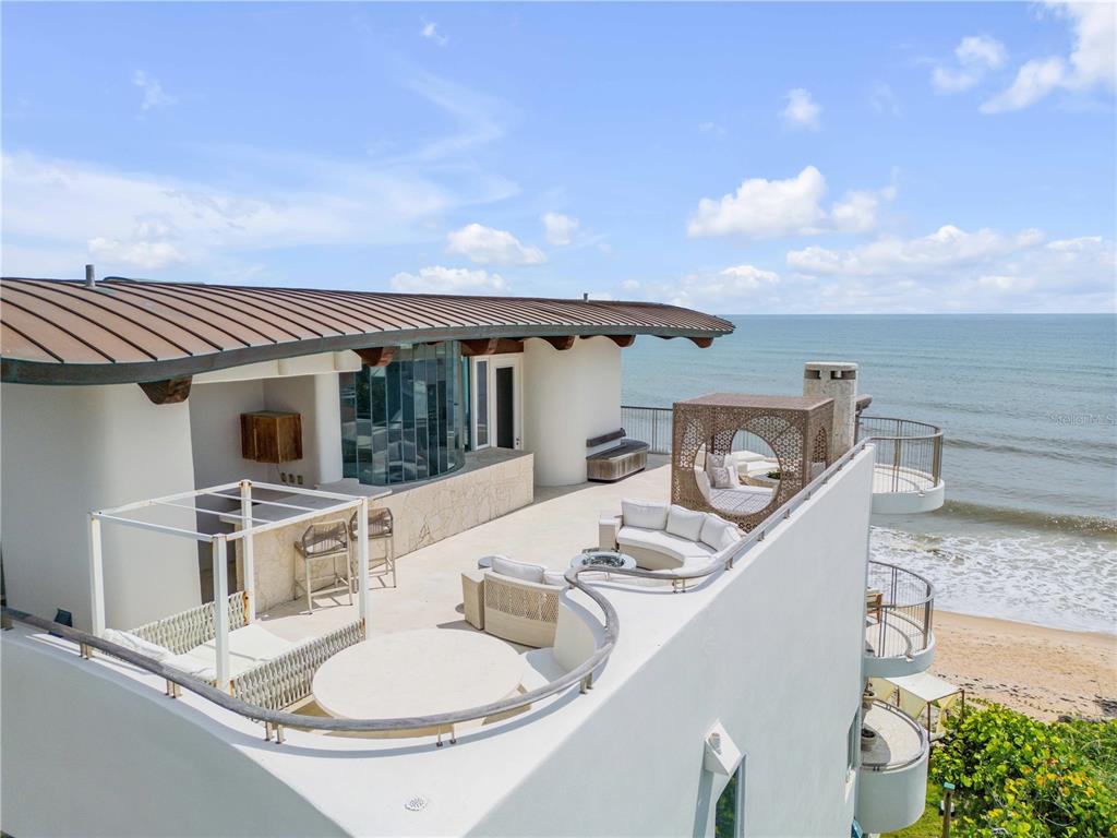 An elevated outdoor terrace features white curved seating, a circular table, and ocean views — 6965 S ATLANTIC AVENUE, NEW SMYRNA BEACH, FL
