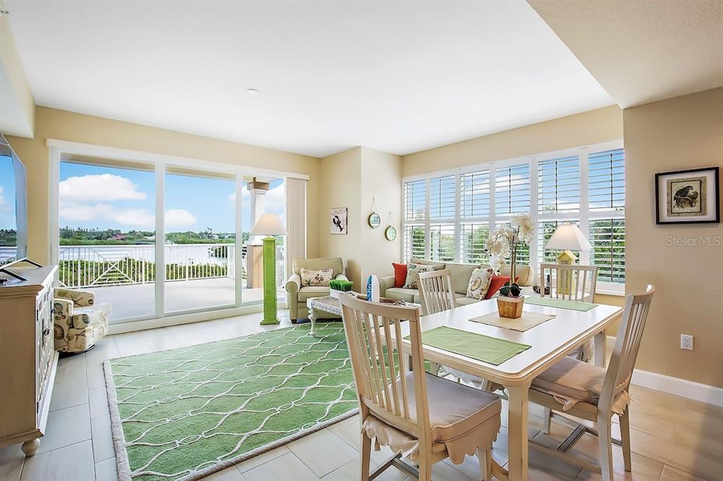 A bright living and dining area features tile floors, a green rug, and waterfront balcony access — 19519 GULF BOULEVARD UNIT 206, INDIAN SHORES, FL