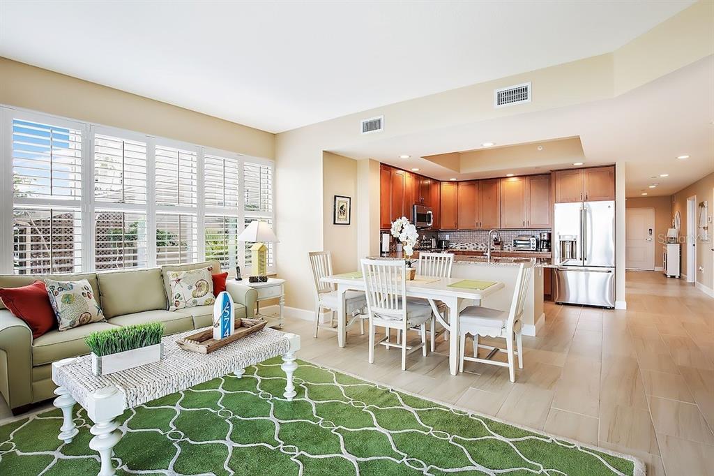 An open-concept living and dining area features light wood floors, a green rug, and kitchen — 19519 GULF BOULEVARD UNIT 206, INDIAN SHORES, FL