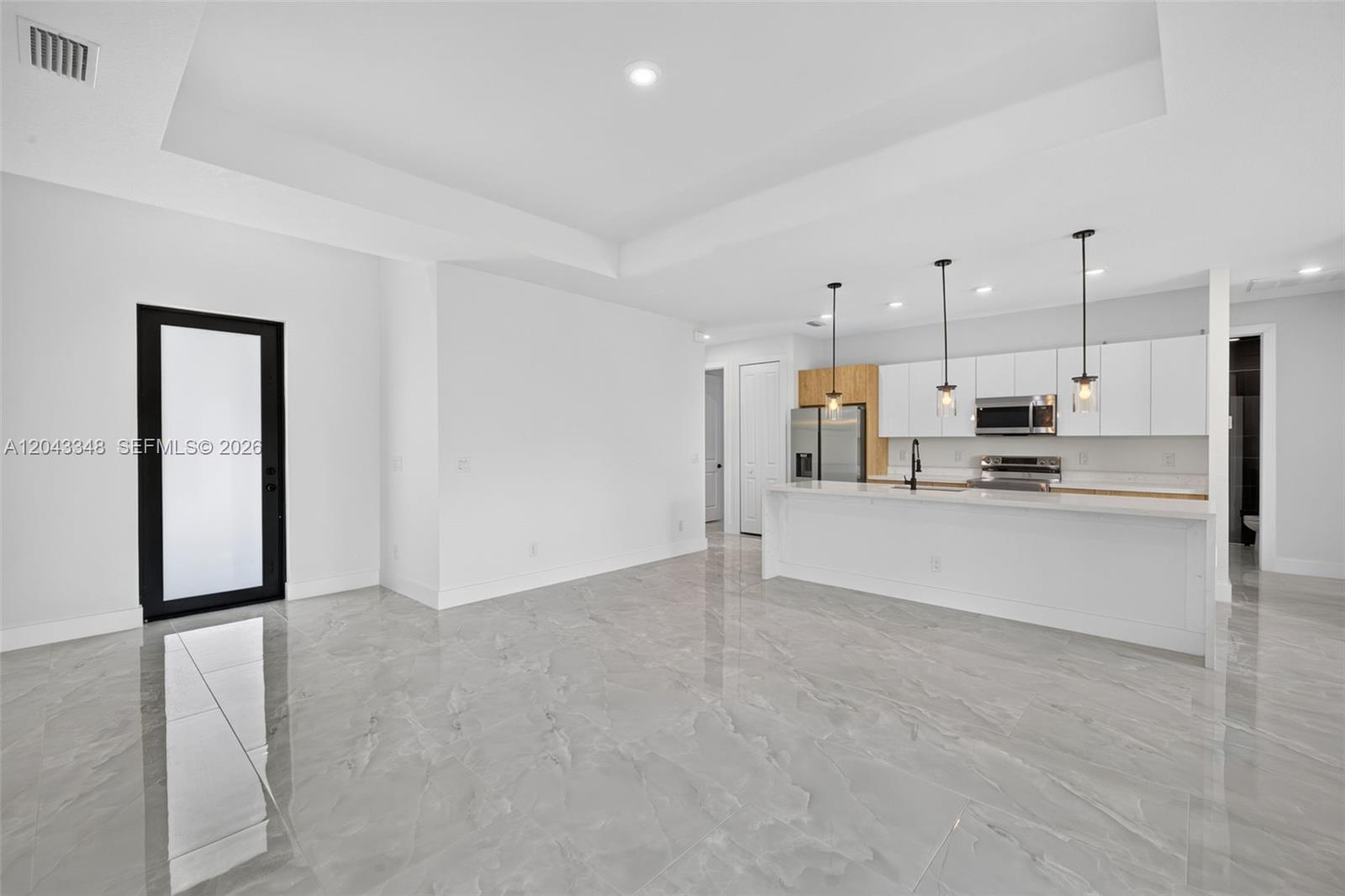 A modern kitchen with white cabinetry and a large island overlooks an open living area — 3216 57th st, Lehigh Acres FL 33971, LEHIGH ACRES, FL
