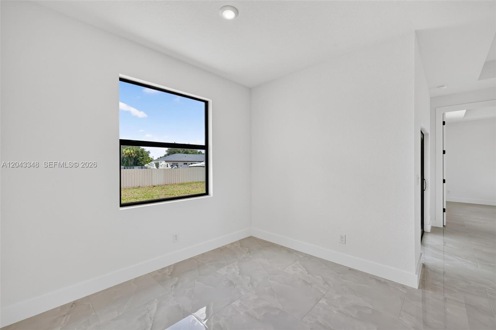 A bright, empty room features white walls, large tile flooring, and a single window — 3216 57th st, Lehigh Acres FL 33971, LEHIGH ACRES, FL
