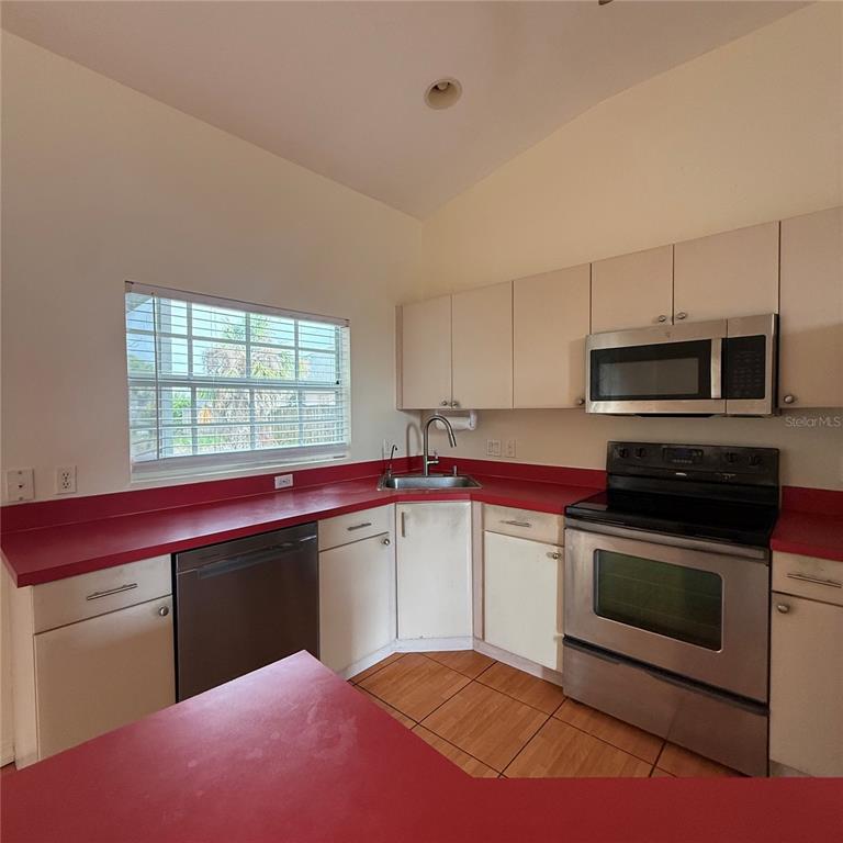 A kitchen features white cabinets, stainless steel appliances, and a bright red countertop — 239 VENETIA AVENUE, NORTH PORT, FL