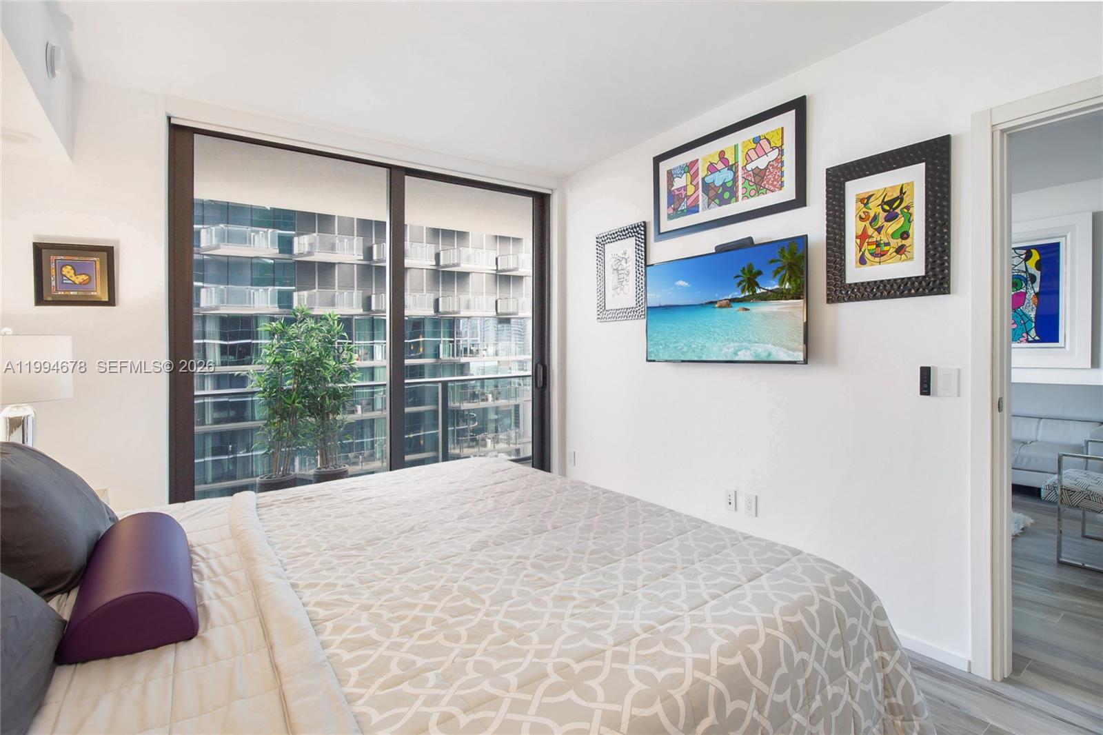 A bedroom features a bed, wall-mounted television, framed artwork, and a sliding glass door — 801 S Miami Ave # 2308, Miami FL 33130, MIAMI, FL