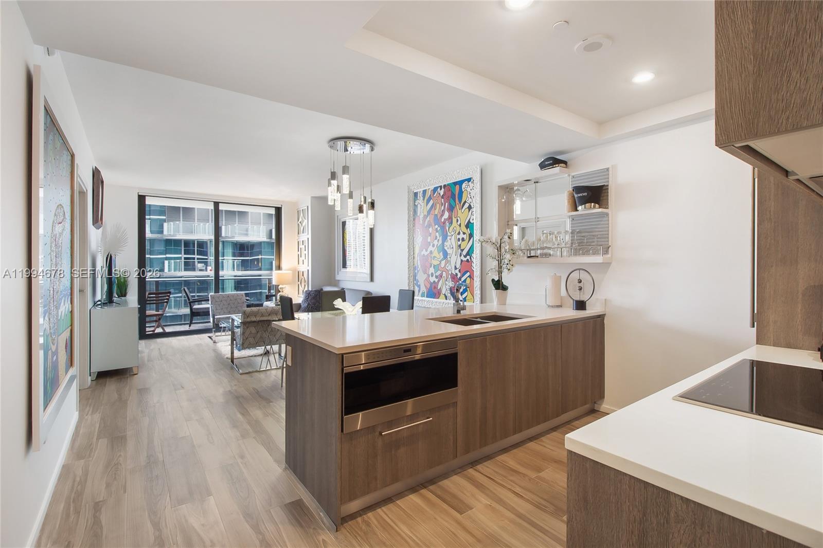 A modern kitchen with wood cabinetry and a quartz island overlooks an open living area — 801 S Miami Ave # 2308, Miami FL 33130, MIAMI, FL