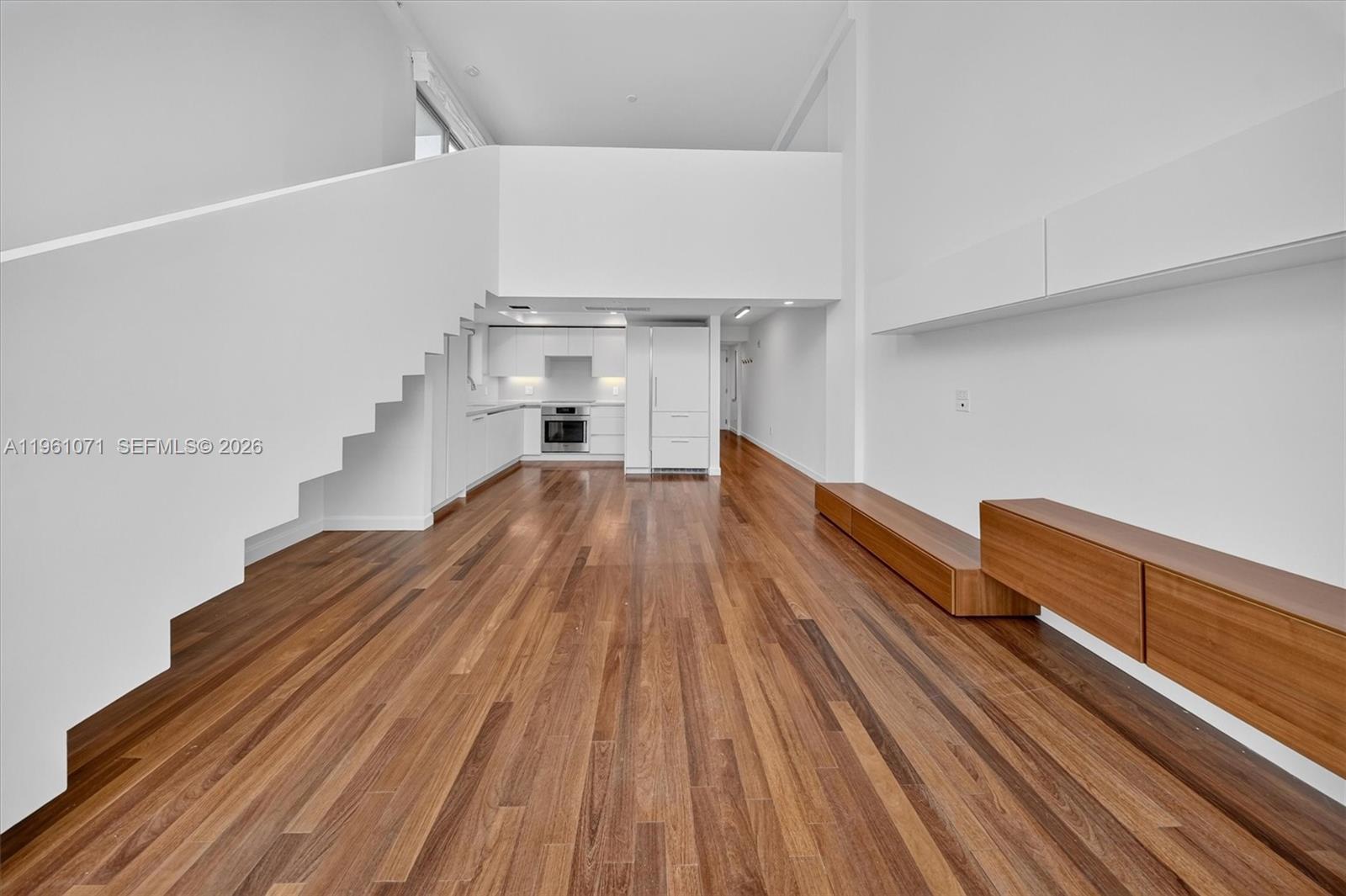 A modern living room features hardwood floors, a white staircase, and a minimalist kitchen — 245 Michigan Ave # 4, Miami Beach FL 33139, MIAMI BEACH, FL