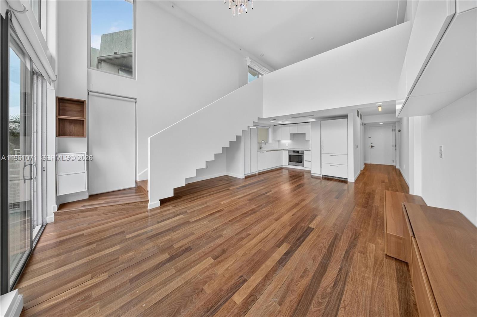 A modern living room features hardwood floors, a white staircase, and an open kitchen — 245 Michigan Ave # 4, Miami Beach FL 33139, MIAMI BEACH, FL