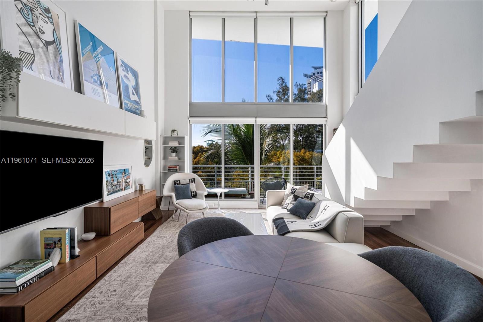 A modern living room features double-height windows, a floating staircase, and a dining area — 245 Michigan Ave # 4, Miami Beach FL 33139, MIAMI BEACH, FL