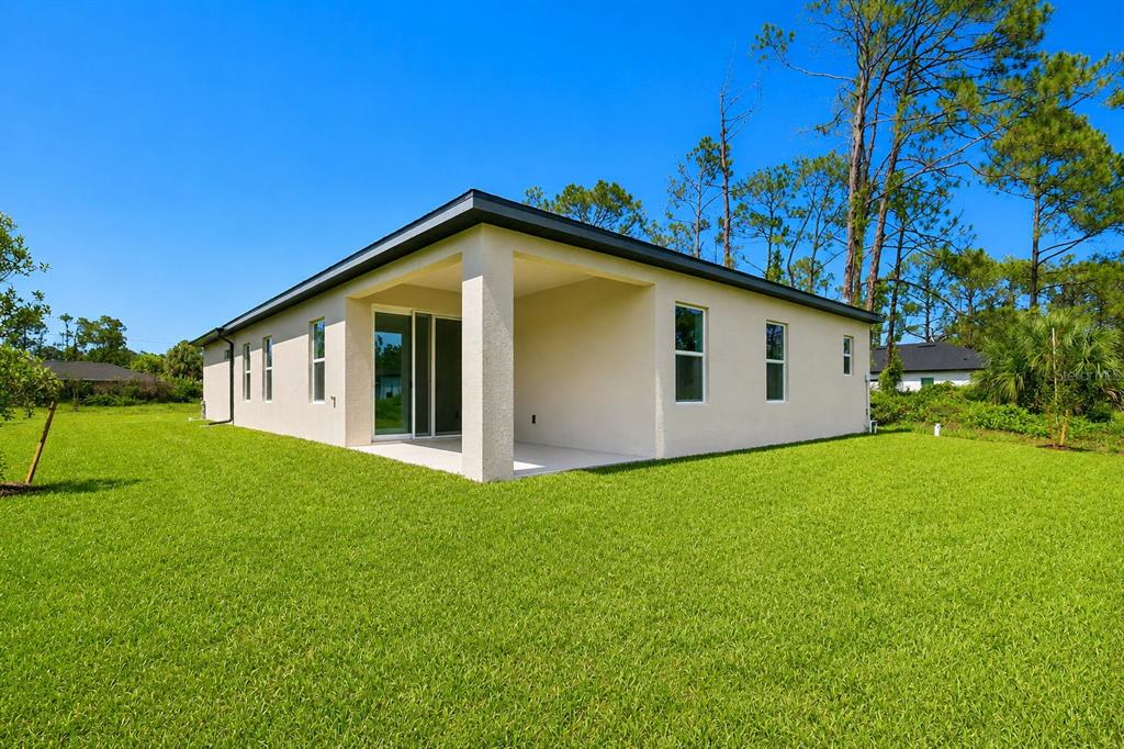 The exterior rear view of a beige house features a covered patio and green lawn — 8211 ELKENBERRY AVENUE, NORTH PORT, FL