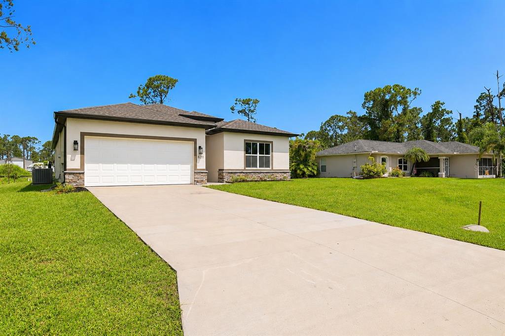 A single-story house with a two-car garage and a concrete driveway under a blue sky — 8211 ELKENBERRY AVENUE, NORTH PORT, FL