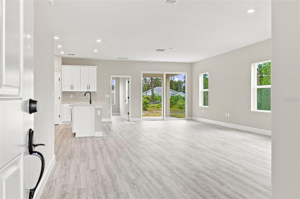 An open-concept living area features light wood-look flooring, white kitchen cabinets, and sliding glass doors — 8211 ELKENBERRY AVENUE, NORTH PORT, FL