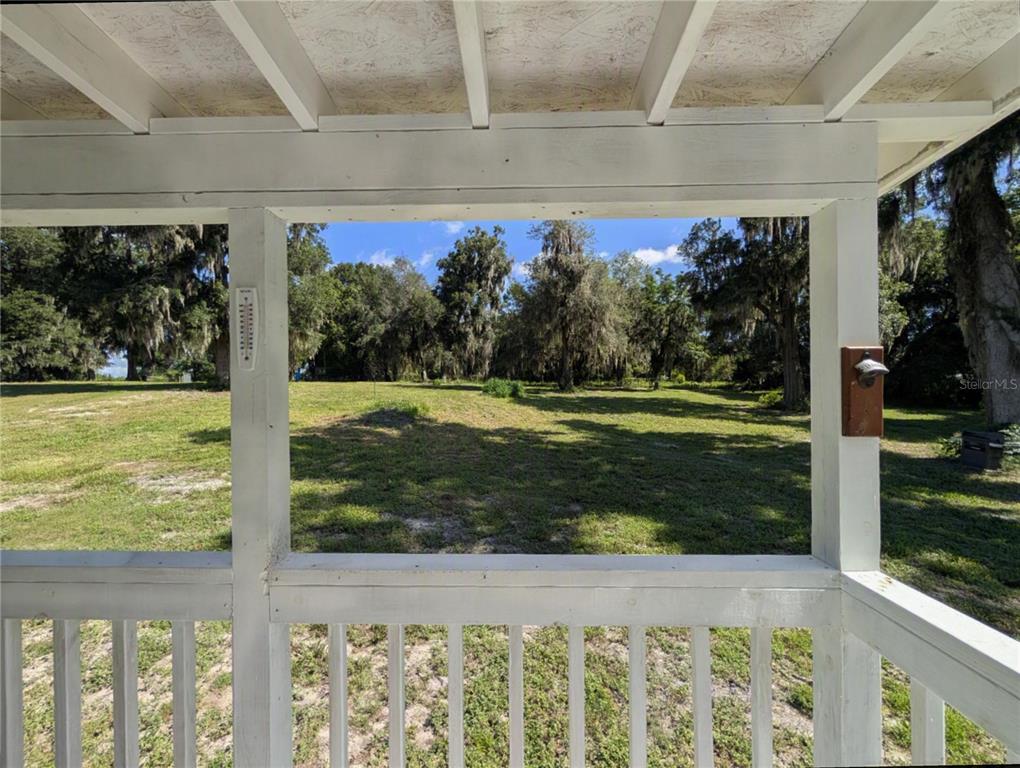 A view of a grassy yard with trees from a white-railed covered porch — 123 AMOS ROAD, CRESCENT CITY, FL