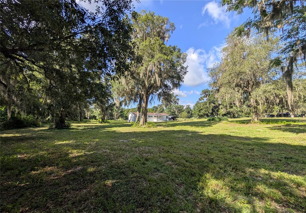 A single-story house sits in the distance on a large, grassy lot with mature trees — 123 AMOS ROAD, CRESCENT CITY, FL