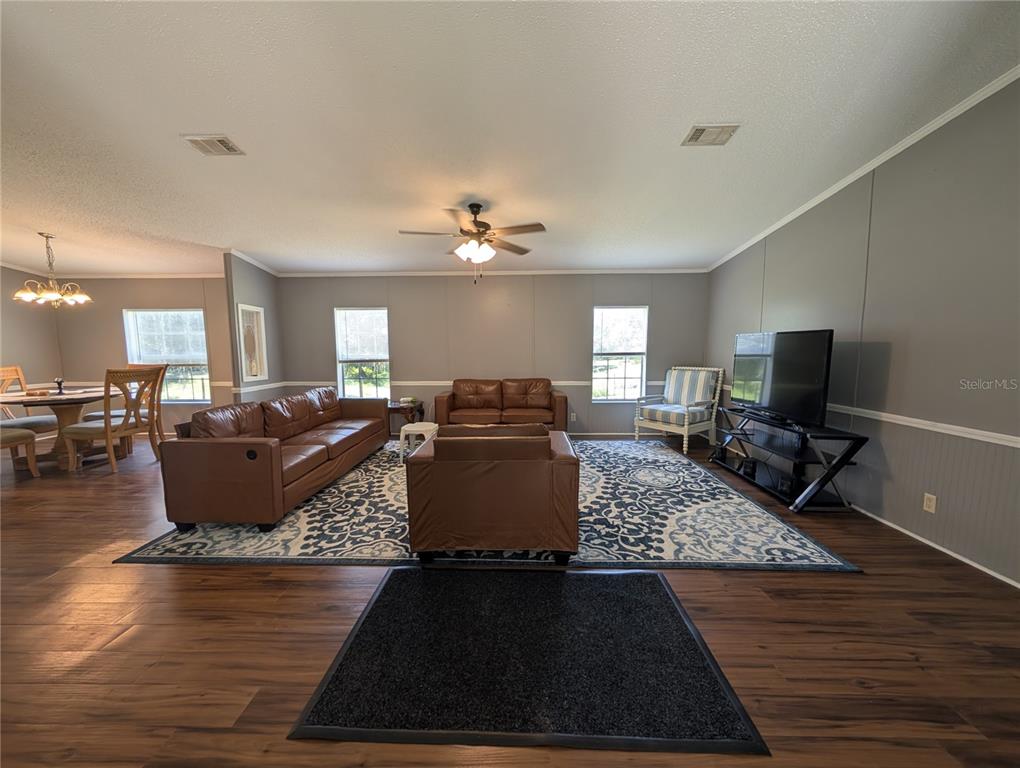 A living room with brown leather furniture, a patterned area rug, and wood-look flooring — 123 AMOS ROAD, CRESCENT CITY, FL