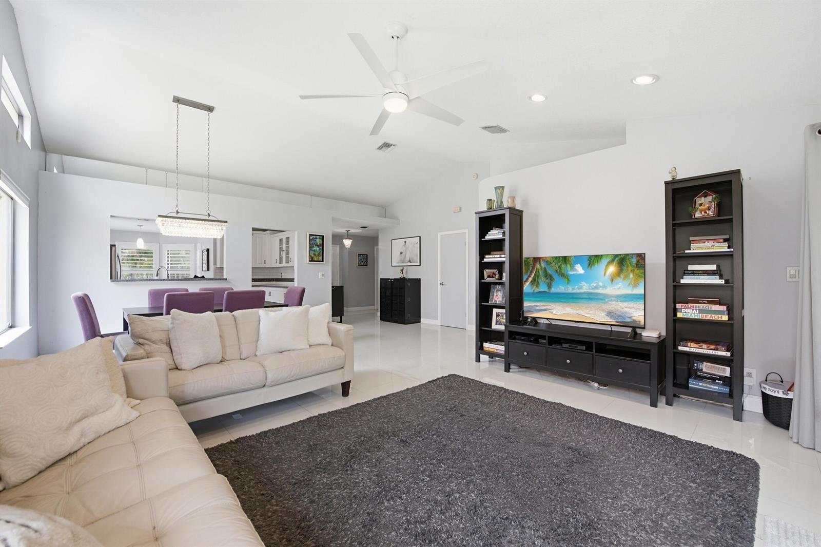 A living room features a white sofa, a dark rug, and a television with shelving — 10577 Mendocino Lane, Boca Raton FL 33428, BOCA RATON, FL