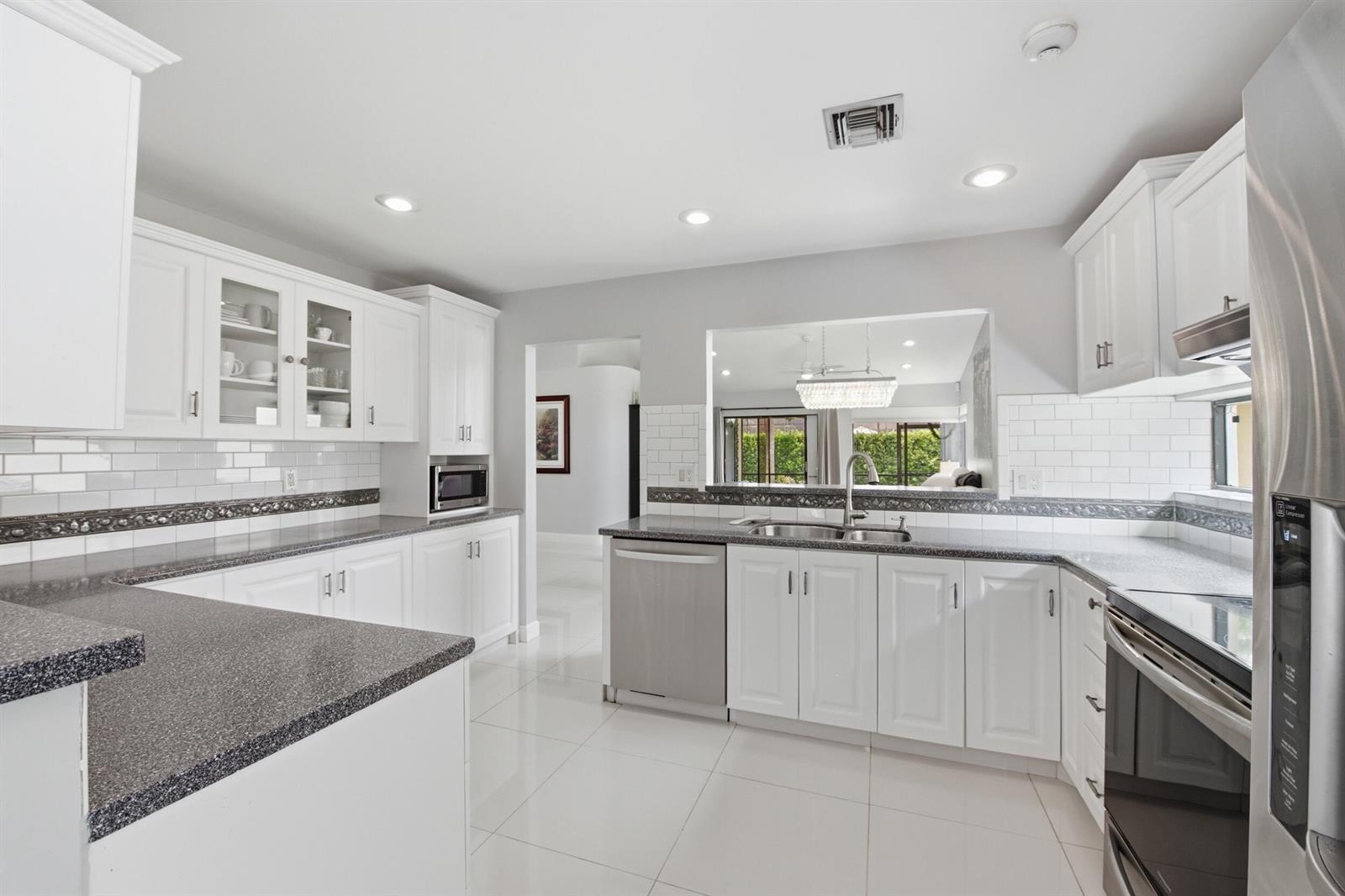 A kitchen with white cabinets, dark granite countertops, stainless steel appliances, and white tile floors — 10577 Mendocino Lane, Boca Raton FL 33428, BOCA RATON, FL