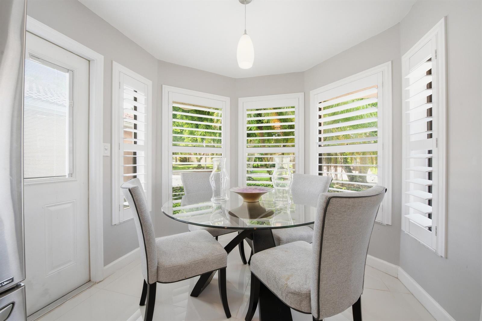 A bright breakfast nook features a glass dining table, four upholstered chairs, and plantation shutters — 10577 Mendocino Lane, Boca Raton FL 33428, BOCA RATON, FL