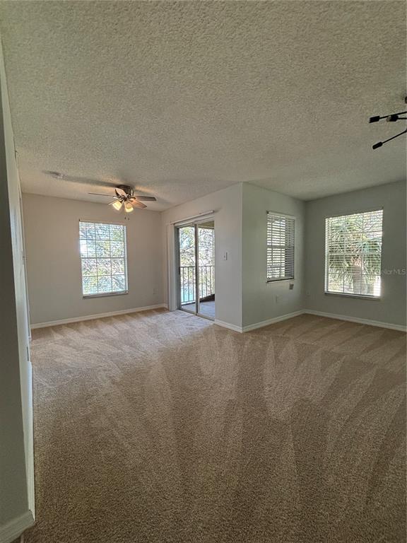 An empty living room features beige carpet, light gray walls, a ceiling fan, and sliding doors — 2690 CORAL LANDINGS BOULEVARD UNIT 538, PALM HARBOR, FL