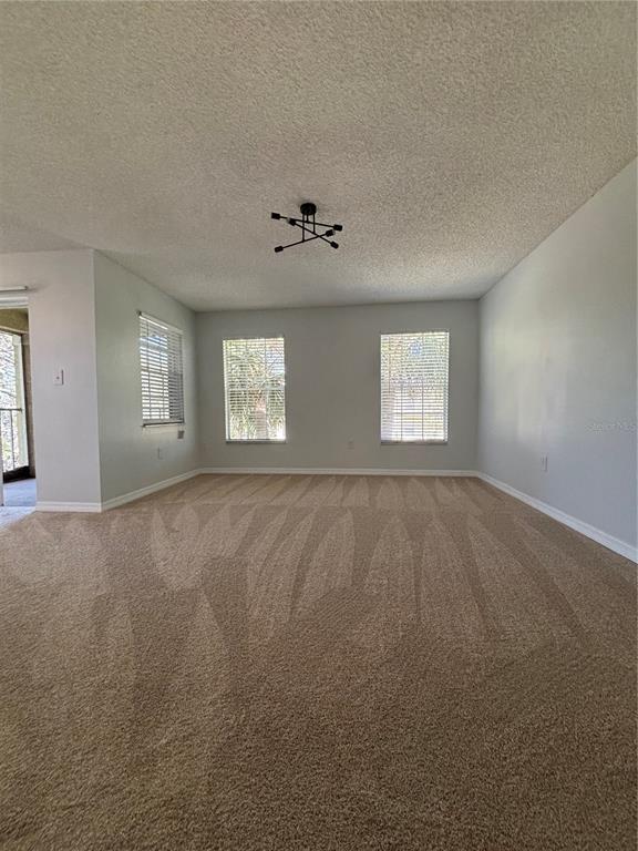 An empty living room with beige carpet, light gray walls, and a modern ceiling light fixture — 2690 CORAL LANDINGS BOULEVARD UNIT 538, PALM HARBOR, FL