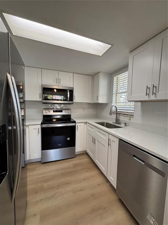 A kitchen with white cabinets, stainless steel appliances, light countertops, and wood-look flooring — 2690 CORAL LANDINGS BOULEVARD UNIT 538, PALM HARBOR, FL