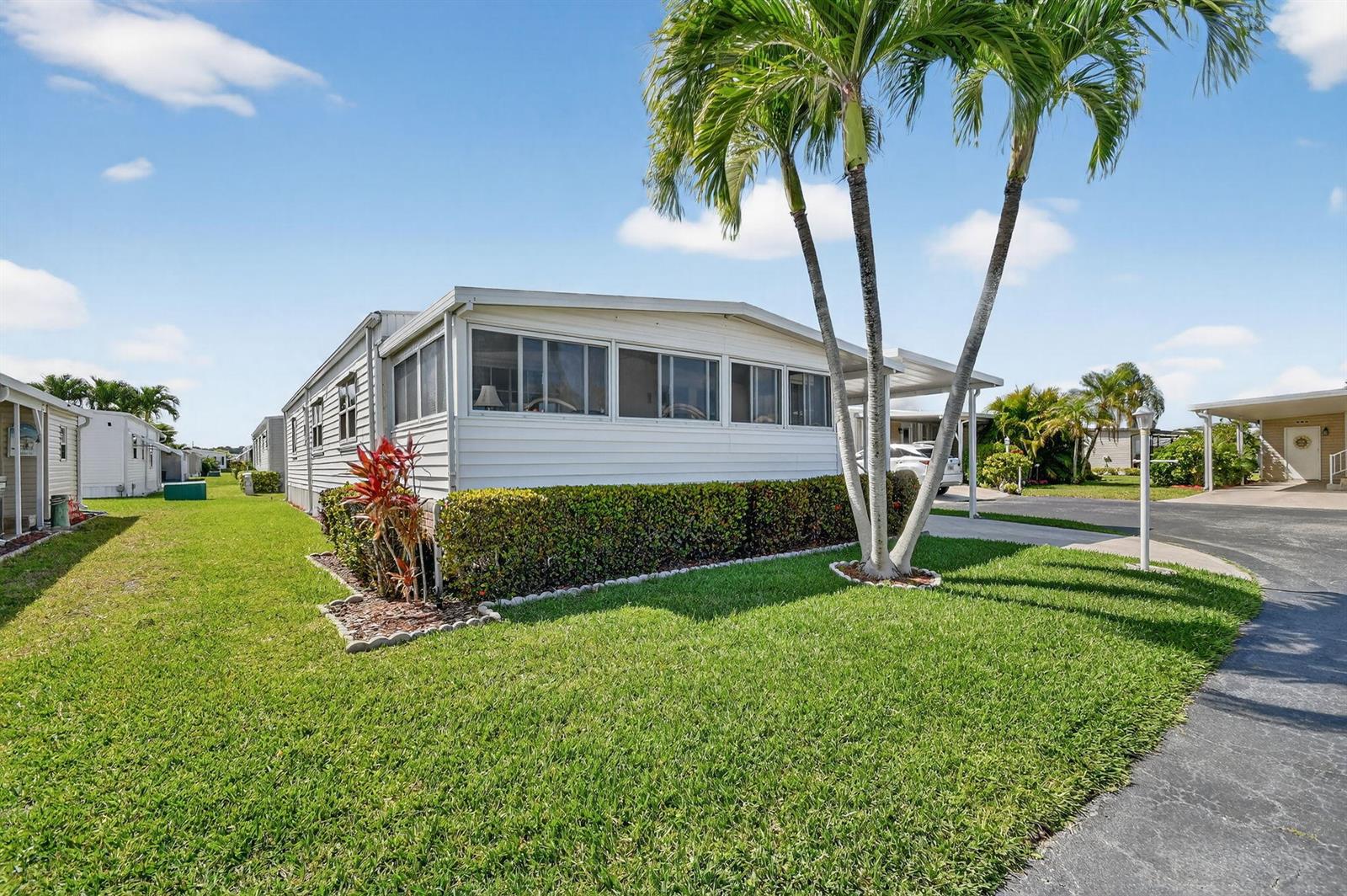 A white manufactured home features a screened-in porch, a manicured lawn, and palm trees — 40008 Humaco Bay, Boynton Beach FL 33436, BOYNTON BEACH, FL