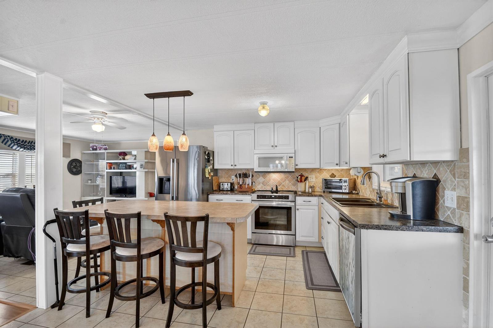 A kitchen features white cabinets, stainless steel appliances, a center island with stools, and tile flooring — 40008 Humaco Bay, Boynton Beach FL 33436, BOYNTON BEACH, FL