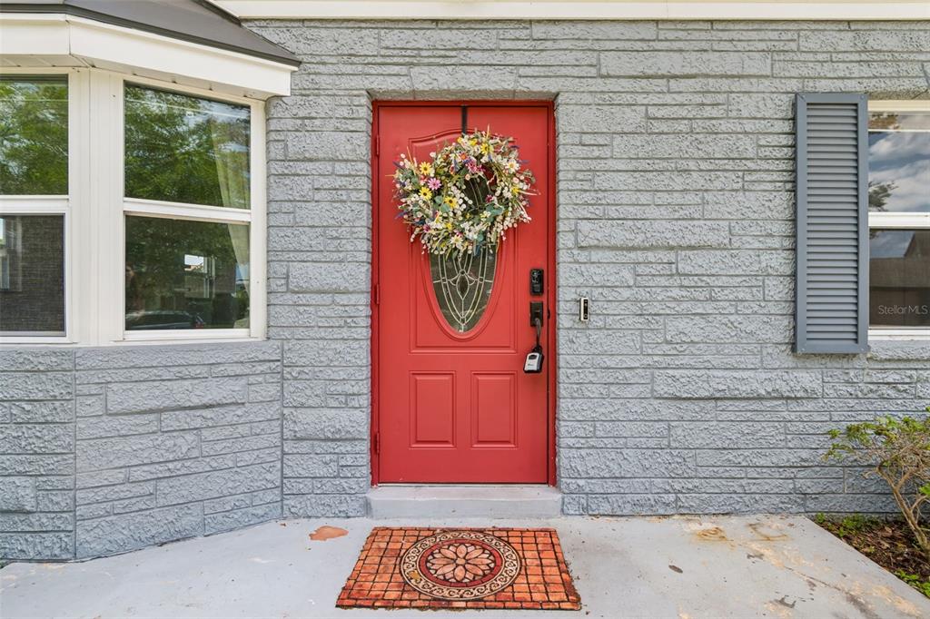 A bright red front door with a floral wreath sits in a gray brick wall — 8043 124TH STREET, SEMINOLE, FL