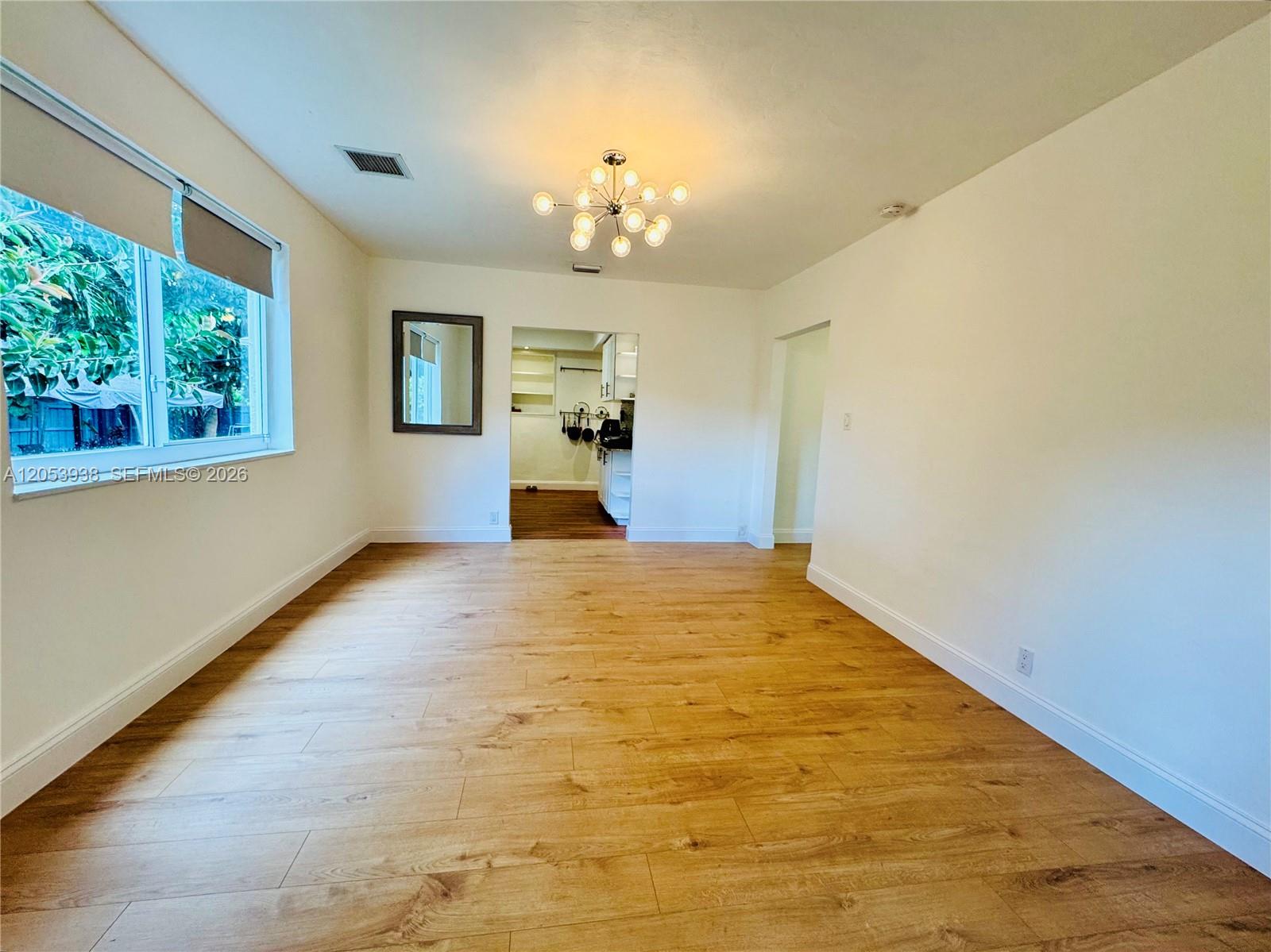 An empty room features light wood-look flooring, white walls, a modern chandelier, and a window — 920 N 26th Ave # 0, Hollywood FL 33020, HOLLYWOOD, FL