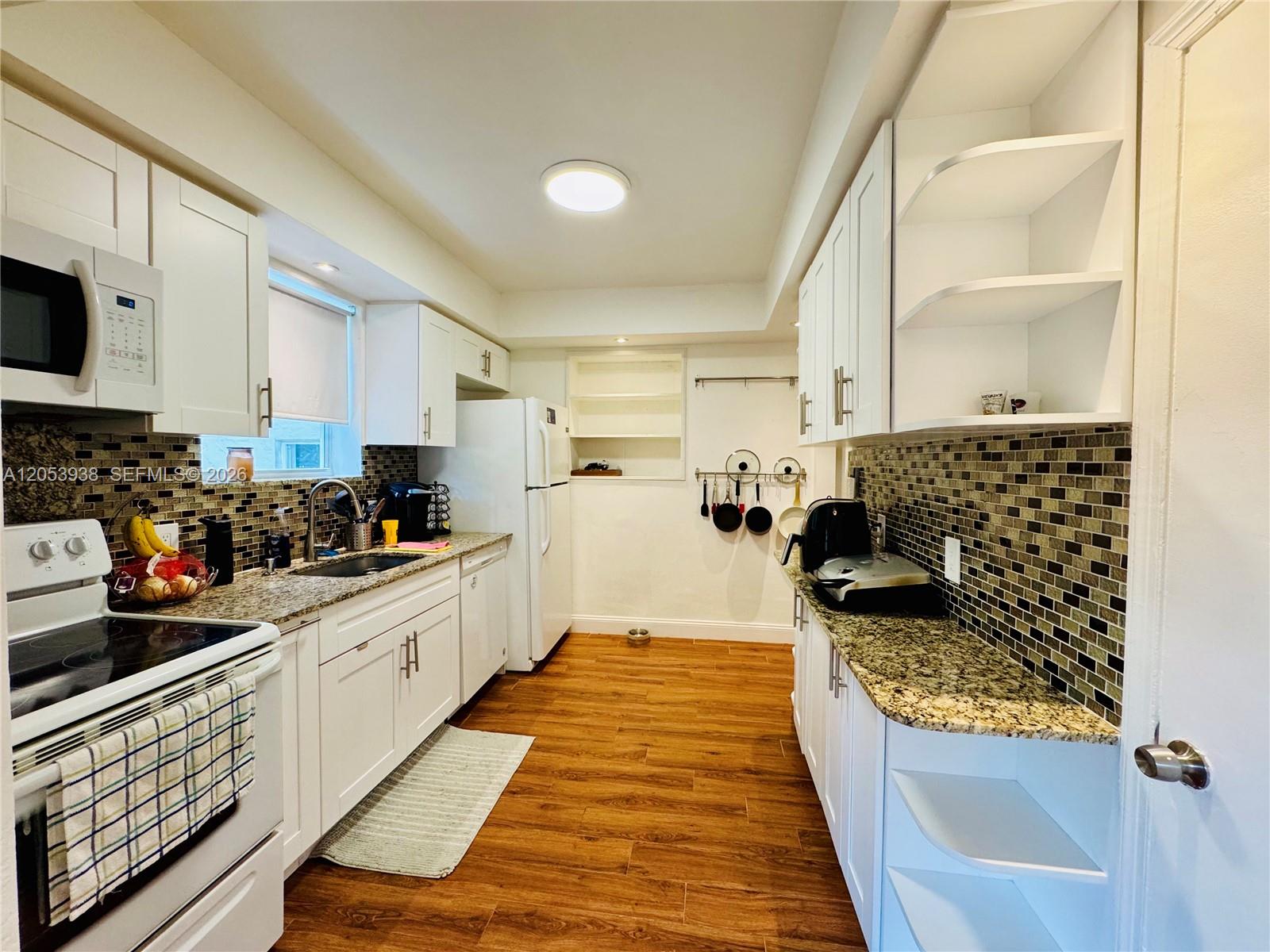 A kitchen features white cabinets, granite countertops, a tiled backsplash, and wood-look flooring — 920 N 26th Ave # 0, Hollywood FL 33020, HOLLYWOOD, FL