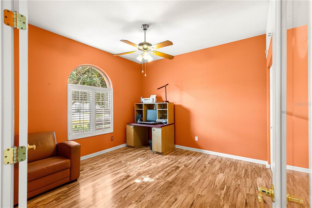 An office with orange walls, wood-look flooring, a desk, a leather chair, and arched window — 2352 NW 58TH TERRACE, OCALA, FL