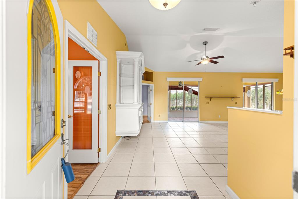 An entryway with yellow walls and tile flooring leads into a living area with a fan — 2352 NW 58TH TERRACE, OCALA, FL