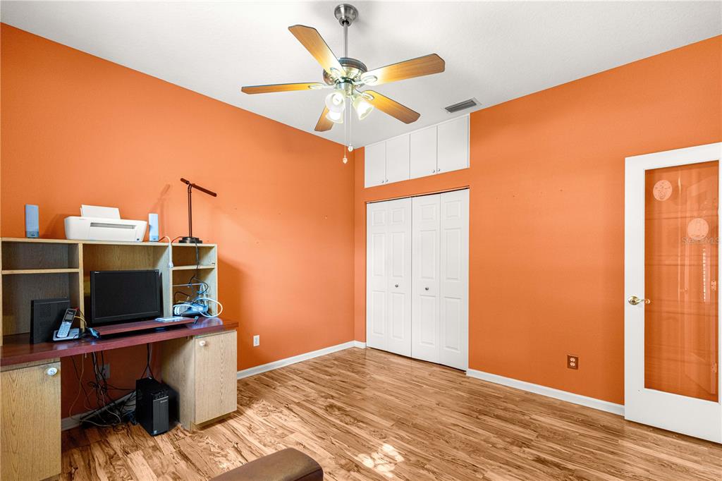 A home office with orange walls, wood-look flooring, a ceiling fan, and a built-in desk — 2352 NW 58TH TERRACE, OCALA, FL