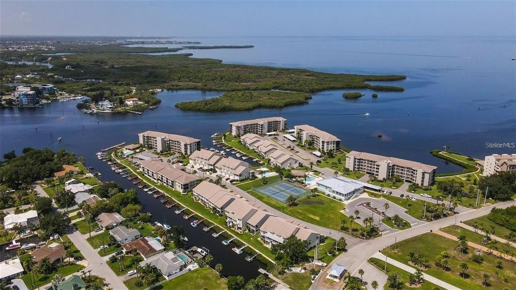 An aerial view shows a waterfront condominium complex with boat slips, tennis courts, and pools — 8222 BRENT STREET, PORT RICHEY, FL