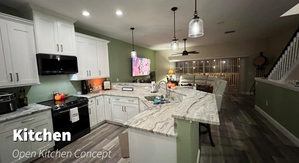 An open-concept kitchen features white cabinetry, stone countertops, and a breakfast bar — 8222 BRENT STREET, PORT RICHEY, FL